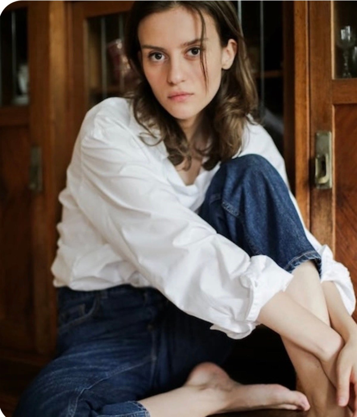 Original soft indoor portrait of a woman sitting by a wooden door before Pica AI enhancement